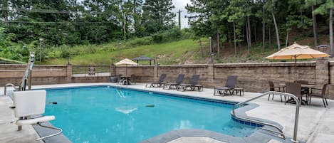 A swimming pool with lounge chairs and umbrellas, surrounded by a stone wall and trees.