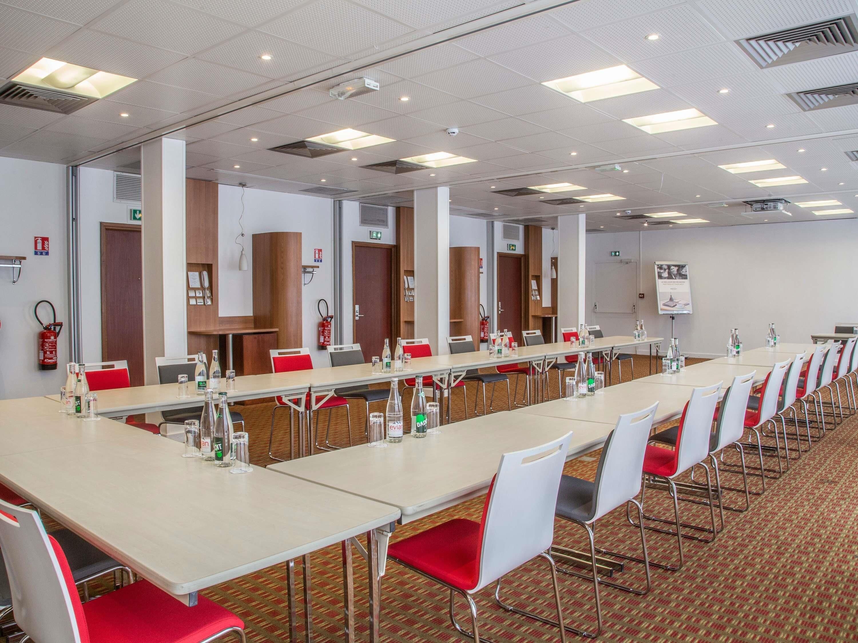A conference room with long tables, chairs, and a projector screen.