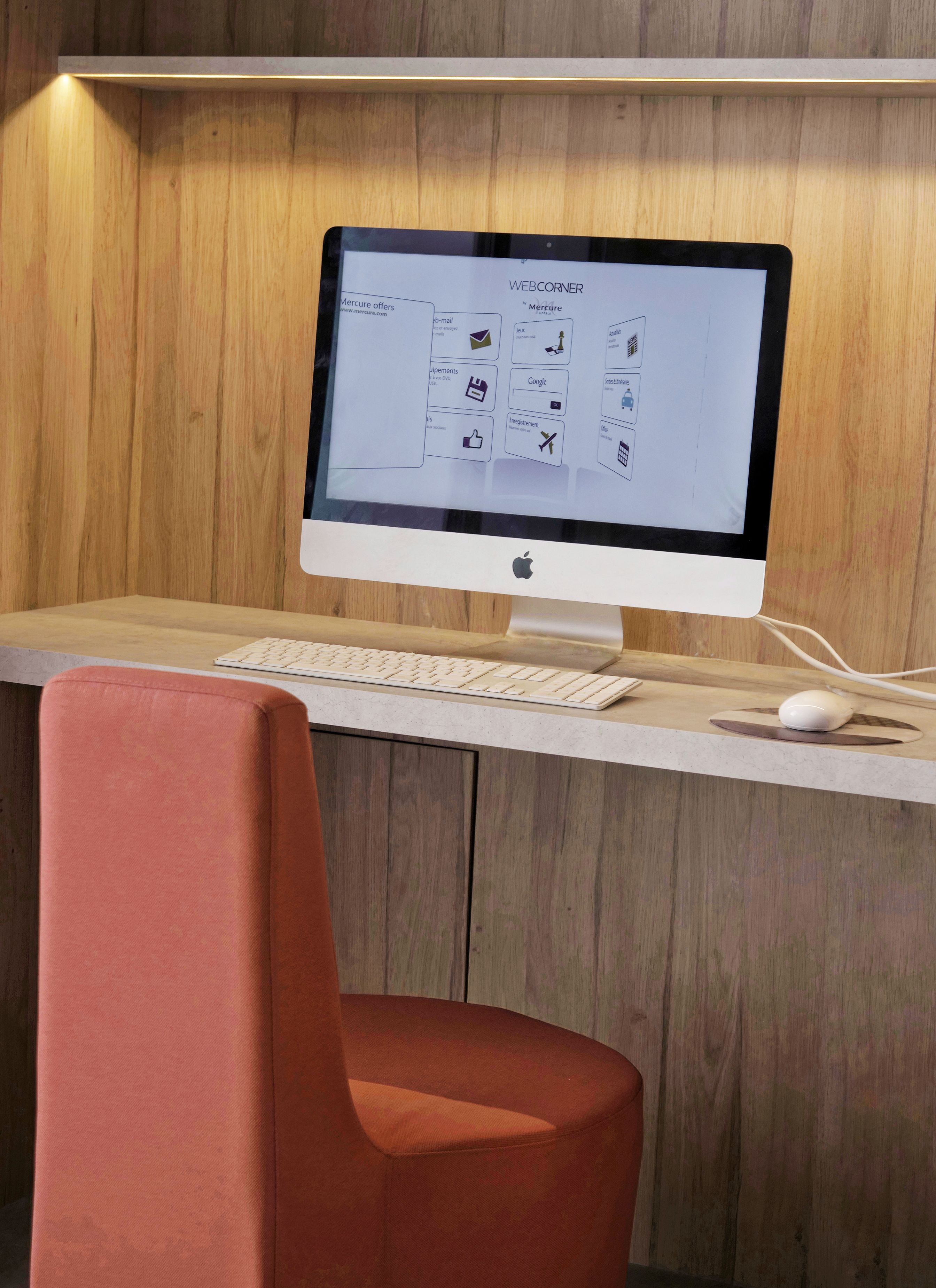 Un espacio de trabajo moderno con un escritorio de madera, un ordenador de Apple, un teclado, un ratón y una silla roja.