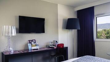 Une chambre d’hôtel comprenant un lit, un bureau avec un téléviseur à écran plat, une lampe et une fenêtre donnant sur l’extérieur.