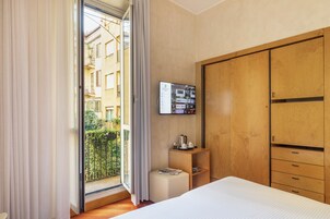 Una camera d'albergo con un letto, un armadio in legno, un tavolino con un bollitore e una televisione a parete.