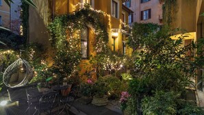 A courtyard with a yellow building, outdoor seating, and string lights. - Hotel Sanpi Milano (Milan)
