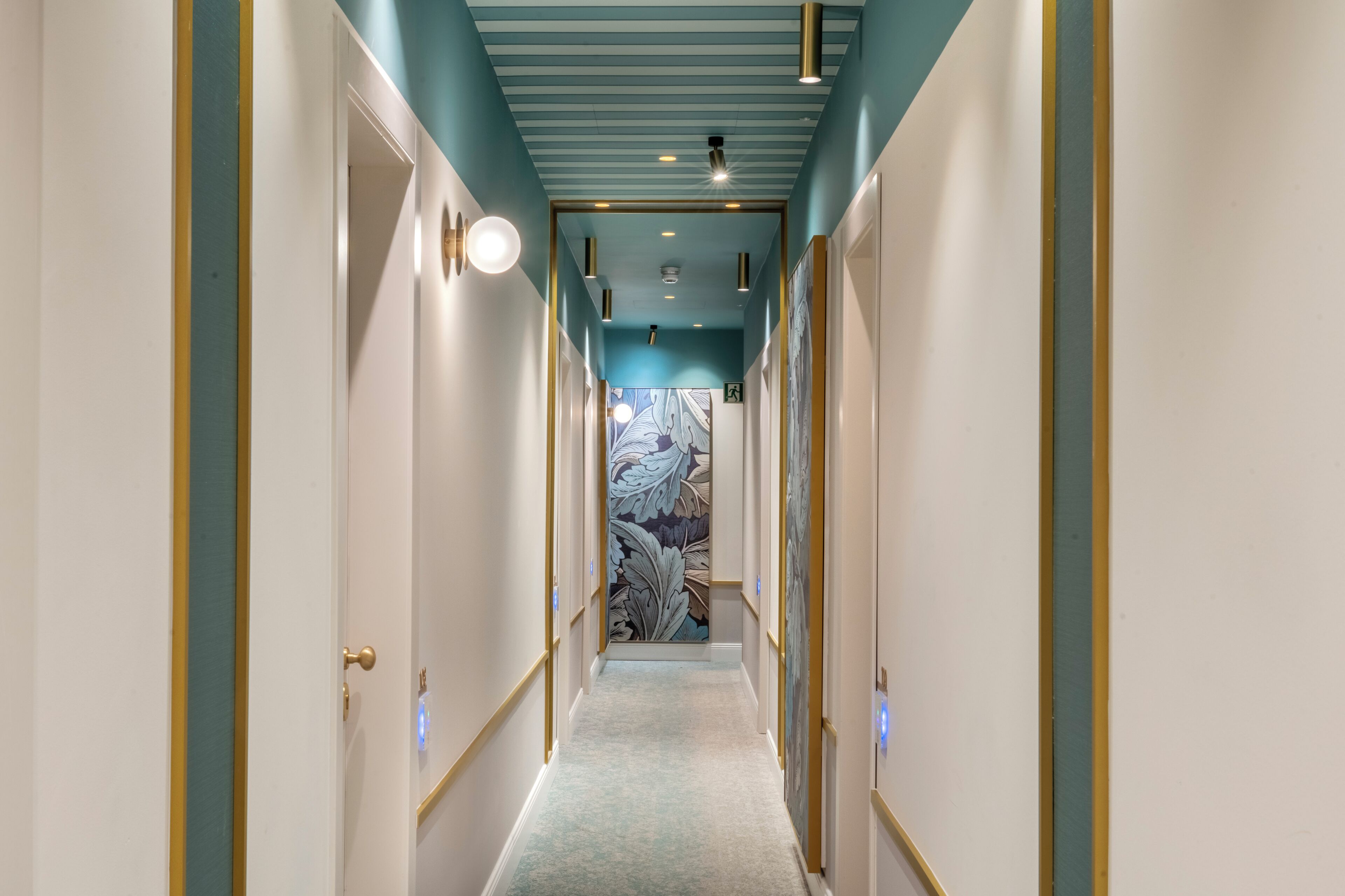 A hallway with a light blue ceiling, white walls, and a patterned wallpaper at the end.