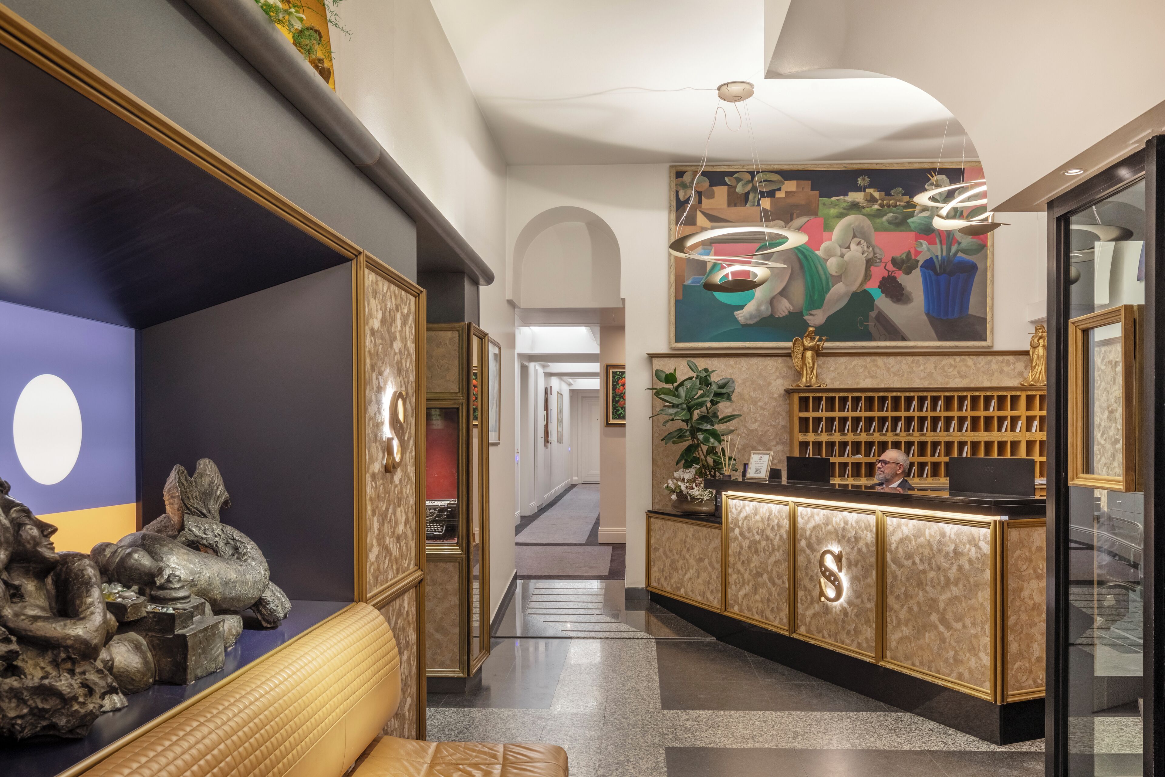 A reception area with a marble counter, a large S-shaped logo, a reception desk, a seating area with a patterned bench, and a mural on the wall.