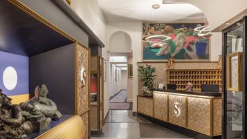 Un espace d’accueil doté d’un comptoir en marbre, d’un grand logo en forme de S, d’un bureau de réception, d’un coin salon avec un banc à motifs et d’une fresque murale.