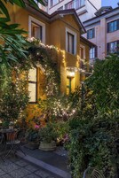 A yellow building with ivy-covered walls and string lights. There are potted plants and outdoor seating.