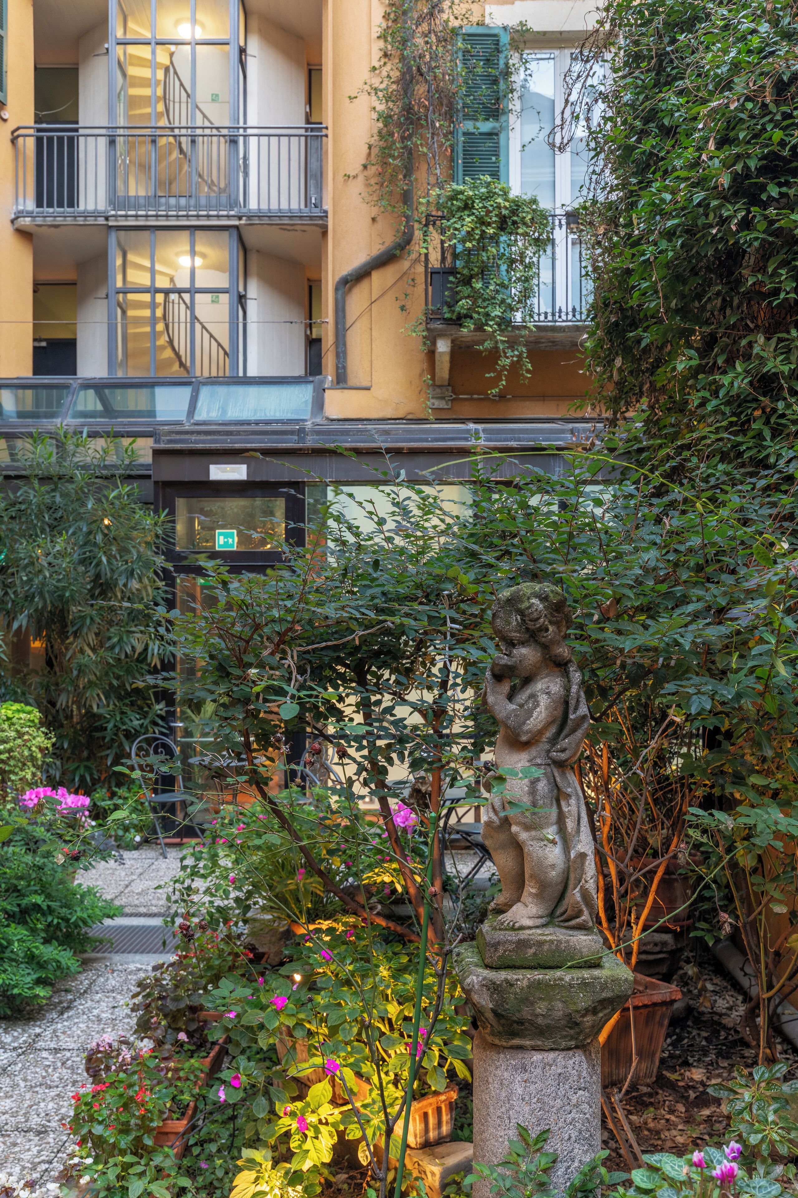 Un cortile con una statua, piante e un edificio con balconi e scale.