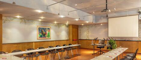 A conference room with a long table, chairs, a projector screen, and a large painting on the wall.