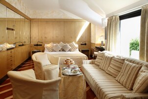 A hotel room with a large bed, a sofa, a chair, a tray with pastries, and a large mirror.