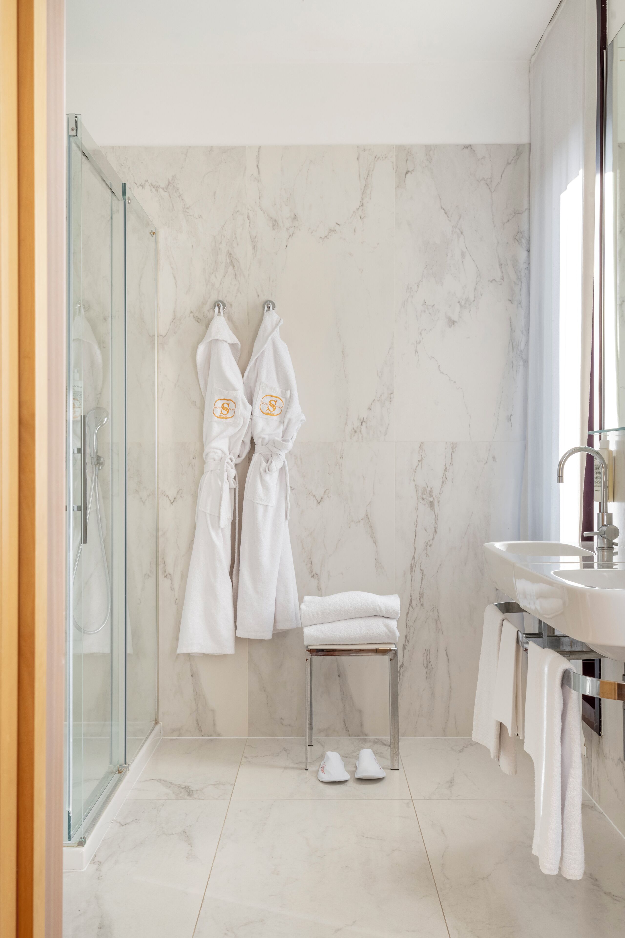 A modern bathroom with a glass shower enclosure, a marble wall, and a white sink.
