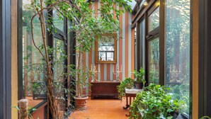 A conservatory with a glass ceiling, potted plants, and a wooden bench. - Hotel Sanpi Milano (Milan)
