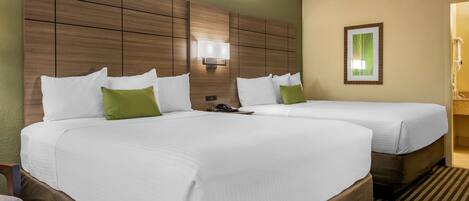 A hotel room with two beds, a wooden headboard, a bedside table, a phone, and a framed picture on the wall.
