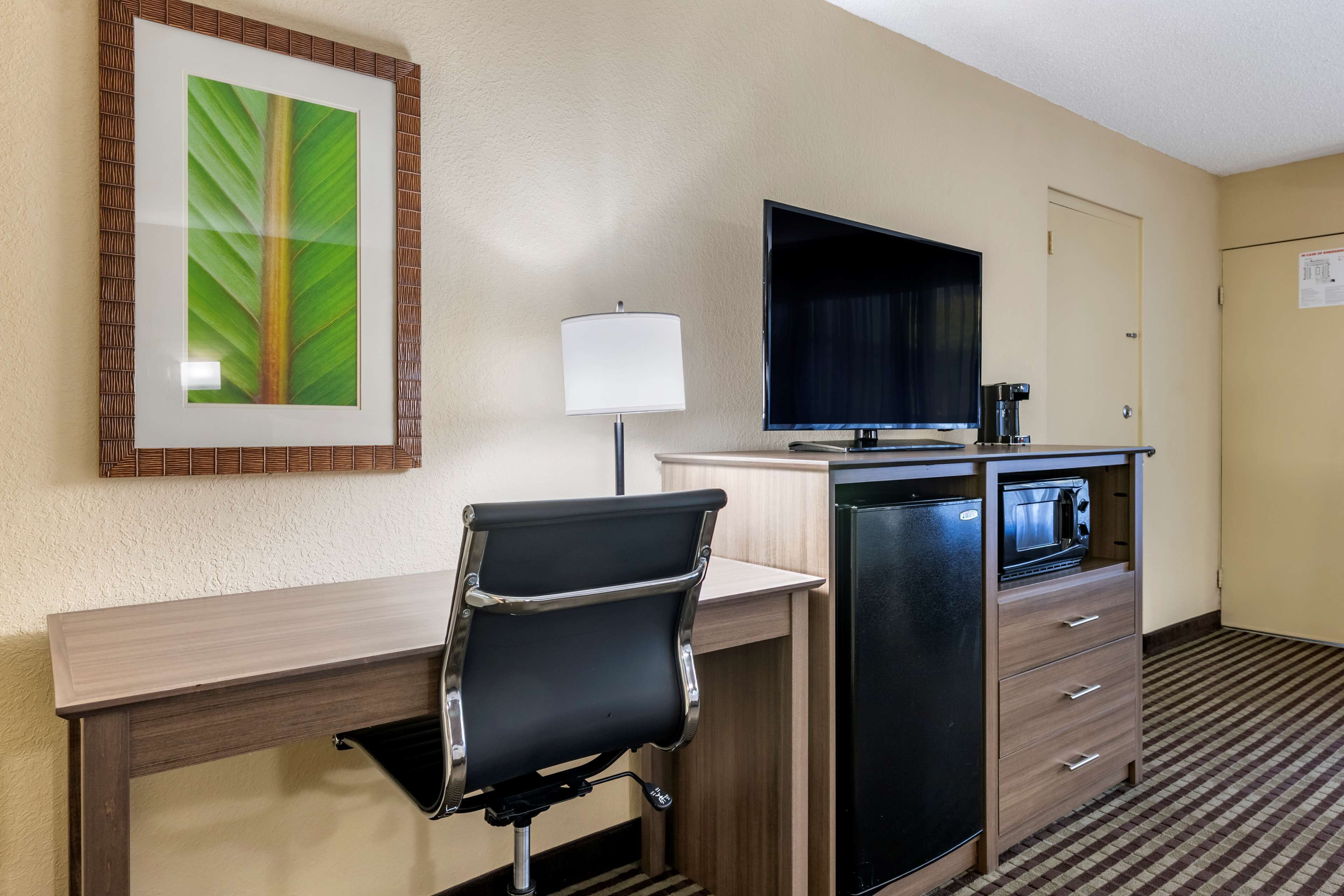 A hotel room with a desk, chair, television, and a minibar.