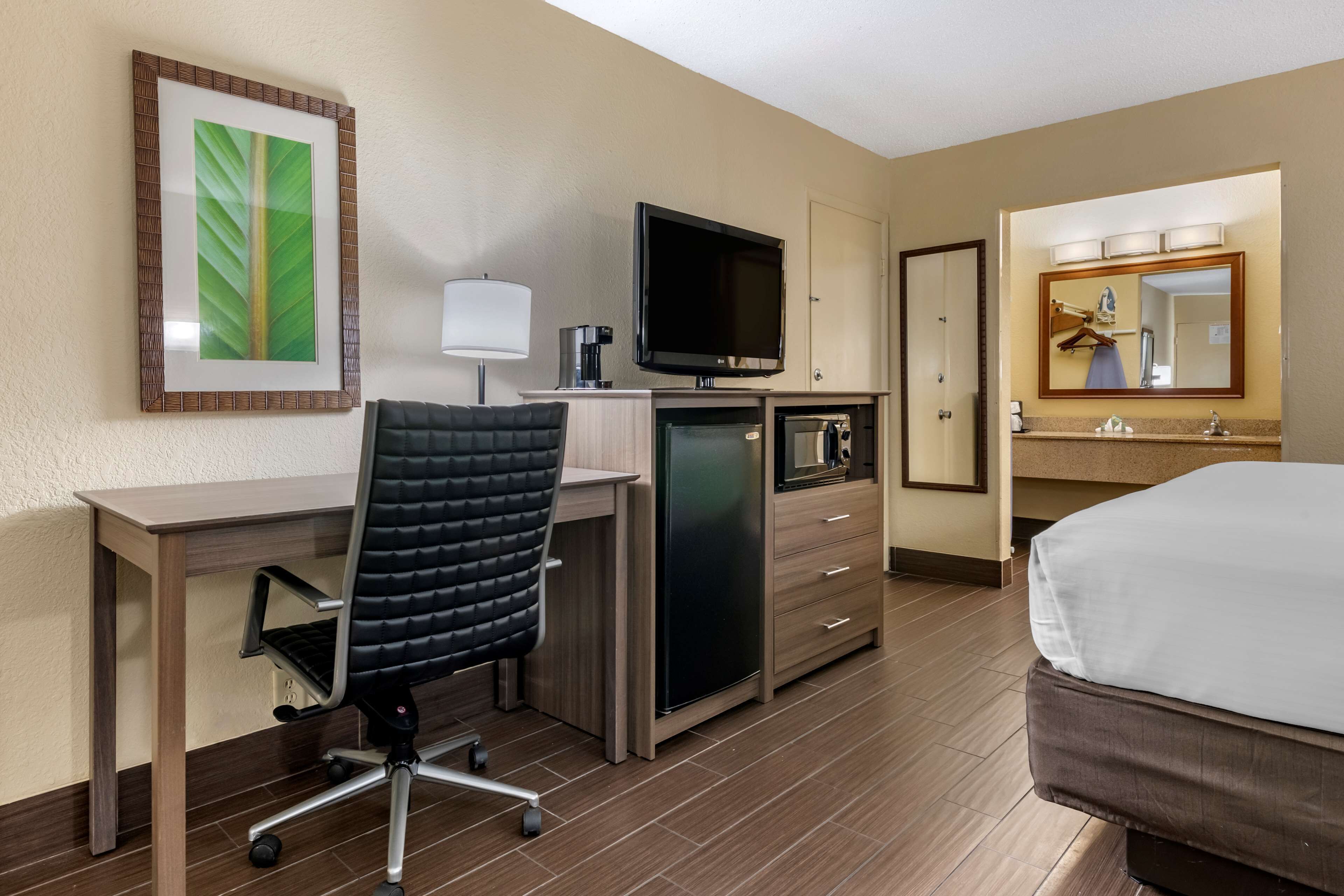 A hotel room with a desk, chair, television, minibar, and a bed.