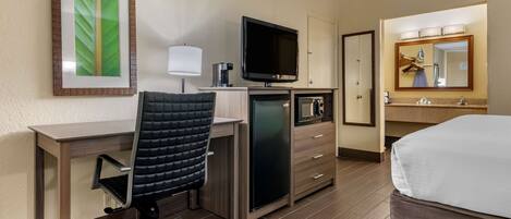 A hotel room with a desk, chair, television, minibar, and a bed.