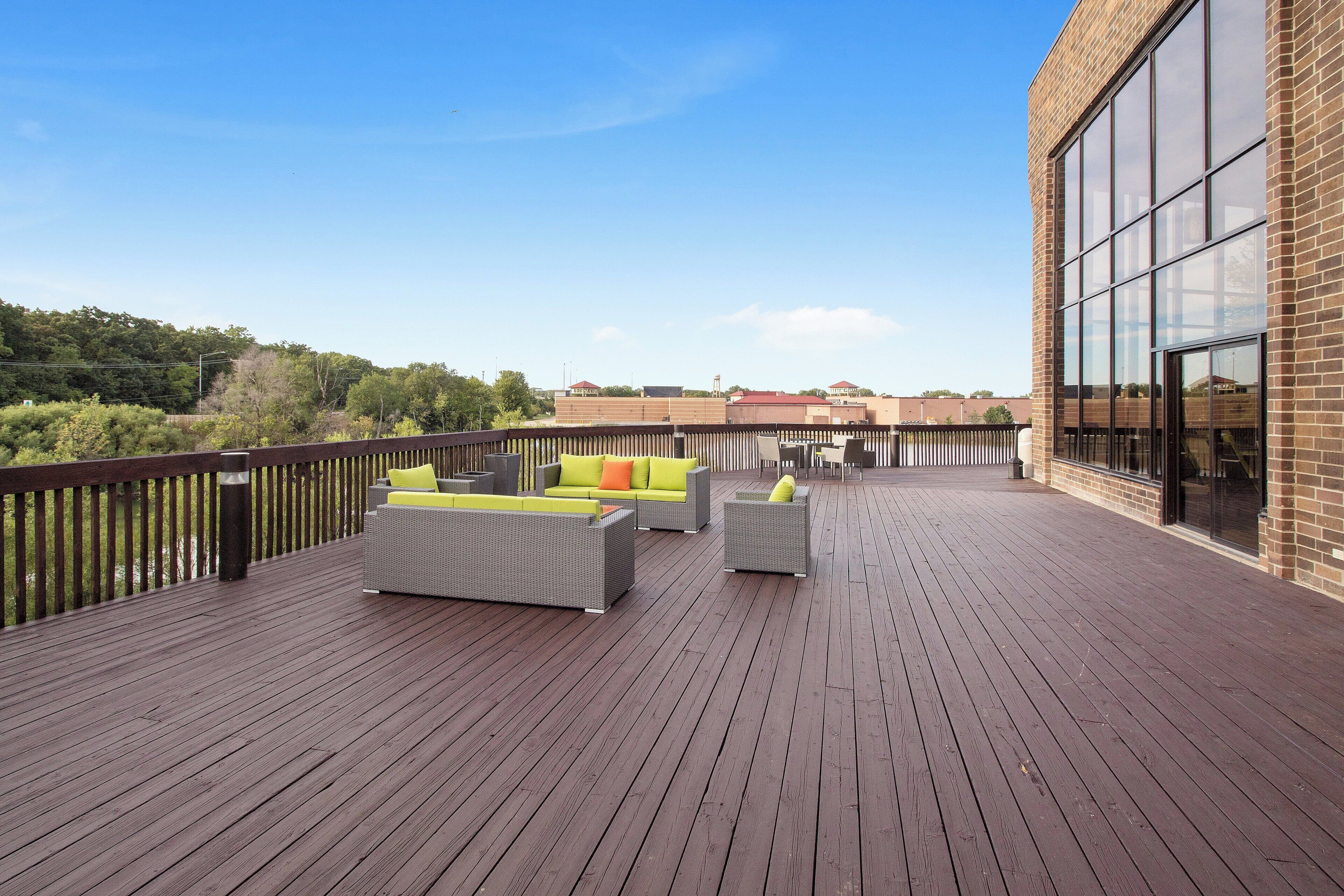 A wooden deck with outdoor furniture, a brick building, and a clear sky.
