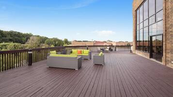 A wooden deck with outdoor furniture, a brick building, and a clear sky.