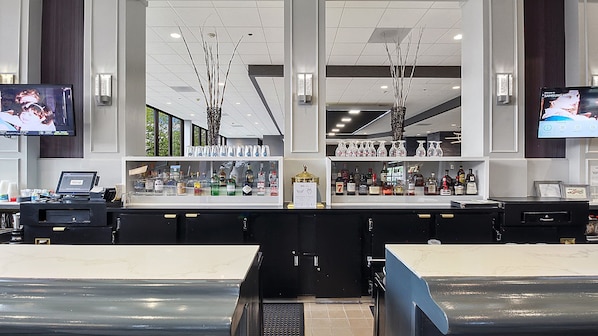 A bar area with a counter, shelves of liquor bottles, and two TVs mounted on the wall. - Holiday Inn Chicago Nw Crystal Lk Conv Ctr by IHG (Crystal Lake)