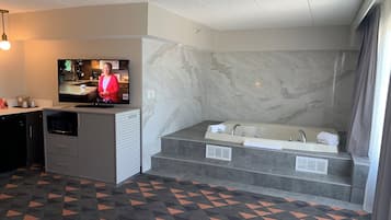 A modern bathroom with a large bathtub, a television, and a herringbone-patterned floor.