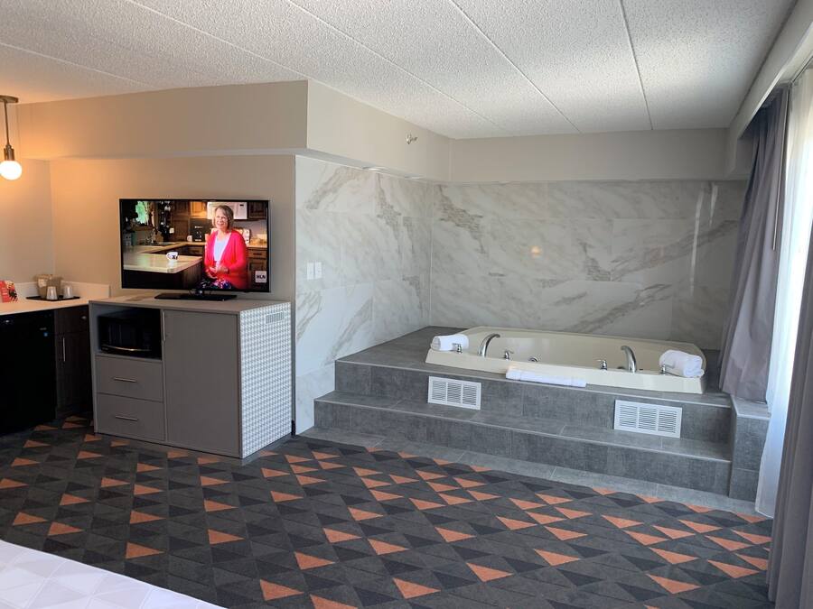 A modern bathroom with a large bathtub, a television, and a herringbone-patterned floor.