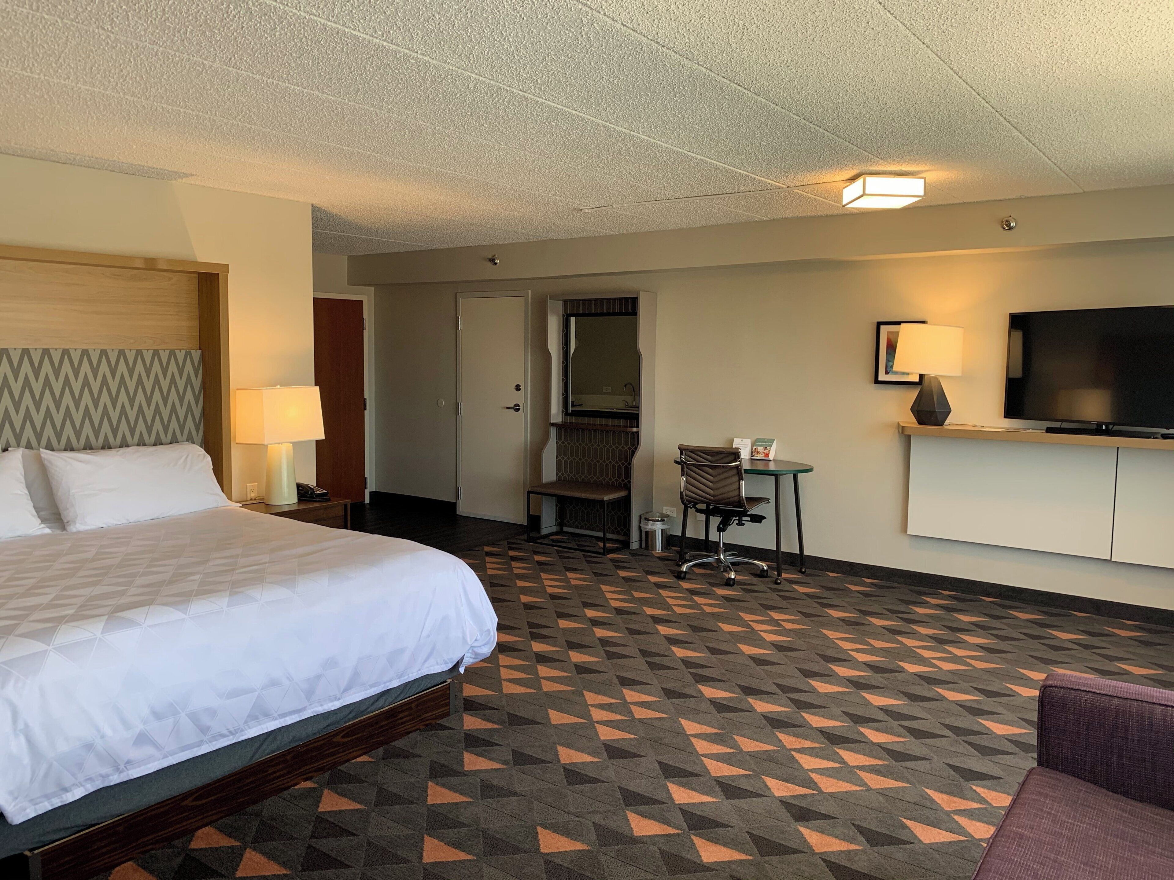 A hotel room with a bed, a desk, a chair, a television, and a bathroom.