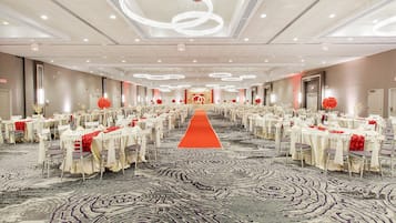 A banquet hall with rows of tables and chairs, a red carpet aisle, and modern lighting fixtures.