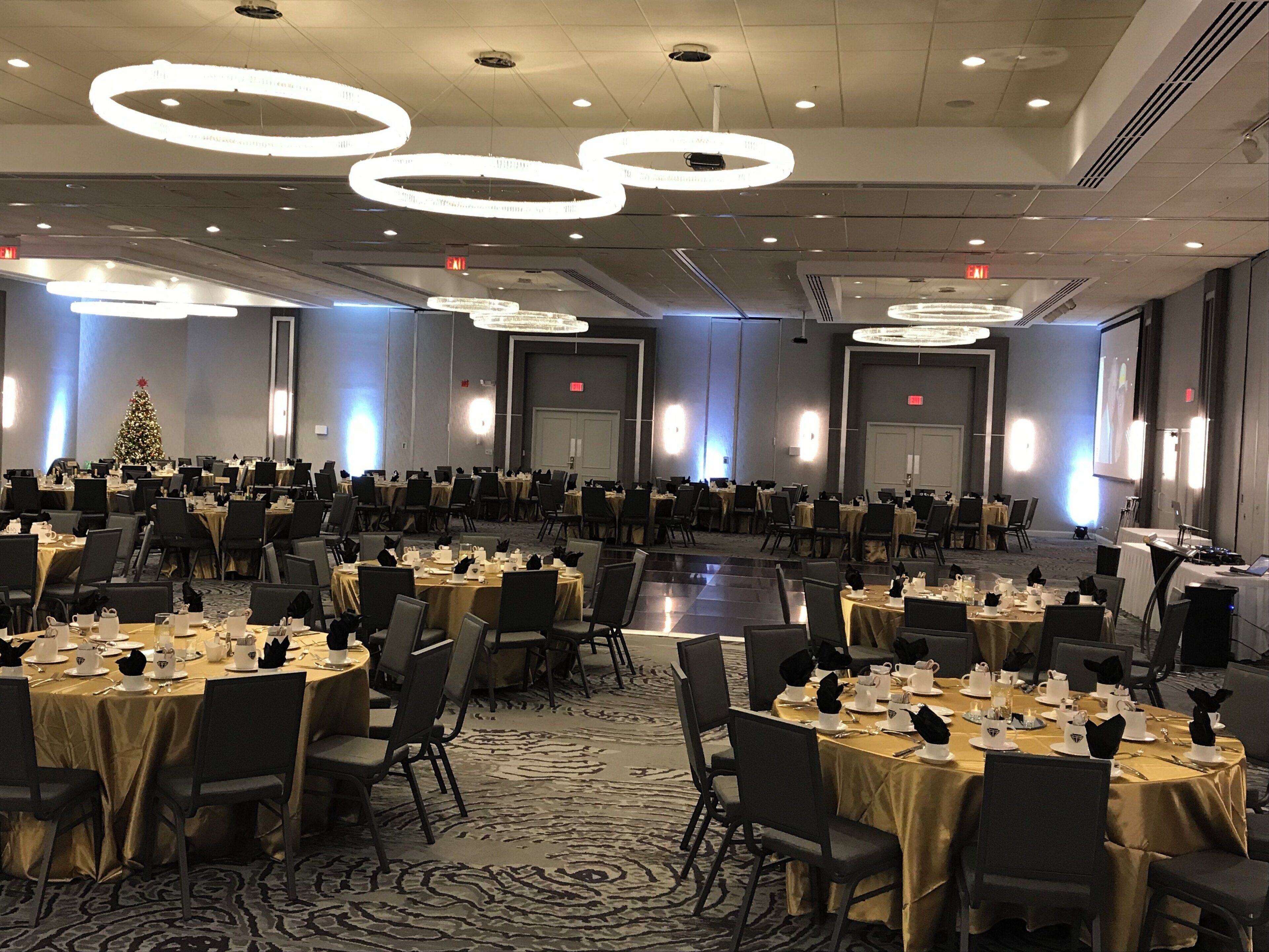 A banquet hall with round tables, chairs, and a Christmas tree.