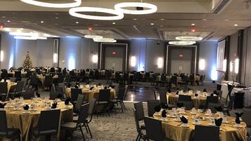 A banquet hall with round tables, chairs, and a Christmas tree.