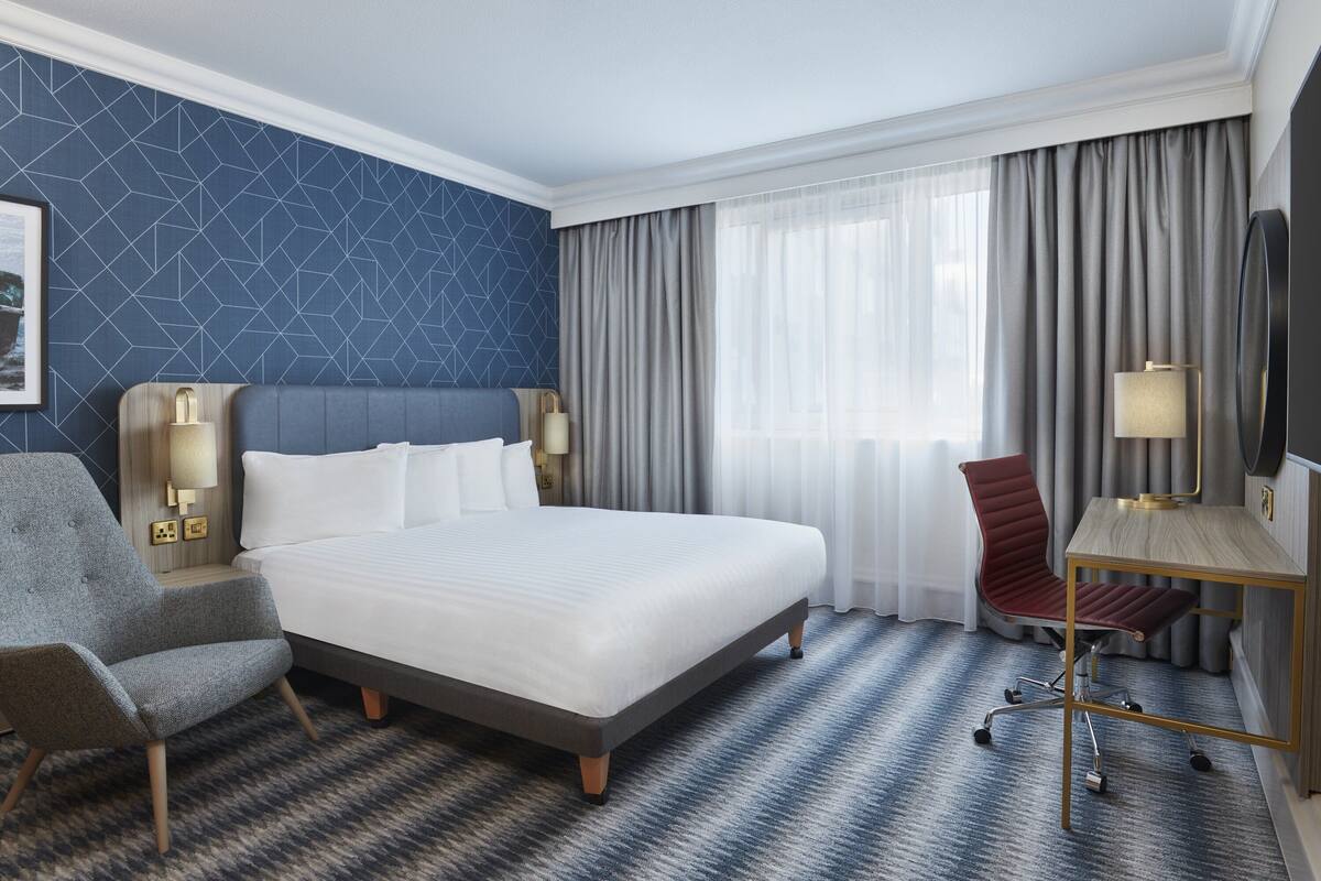 Une chambre d’hôtel avec un grand lit, un bureau, une chaise et un téléviseur.