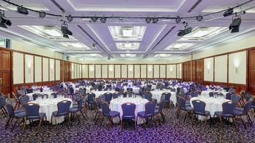 A large conference room with round tables and chairs, equipped with ceiling-mounted projectors and lighting.