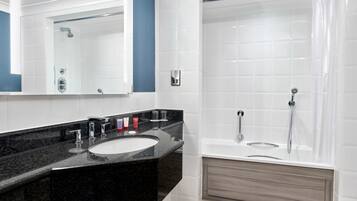 A modern bathroom with a black granite sink, white tiles, a large mirror, and a walk-in shower.