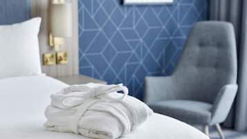Una cama bien hecha con una toalla blanca doblada, un sillón gris y una pared con estampado geométrico azul.