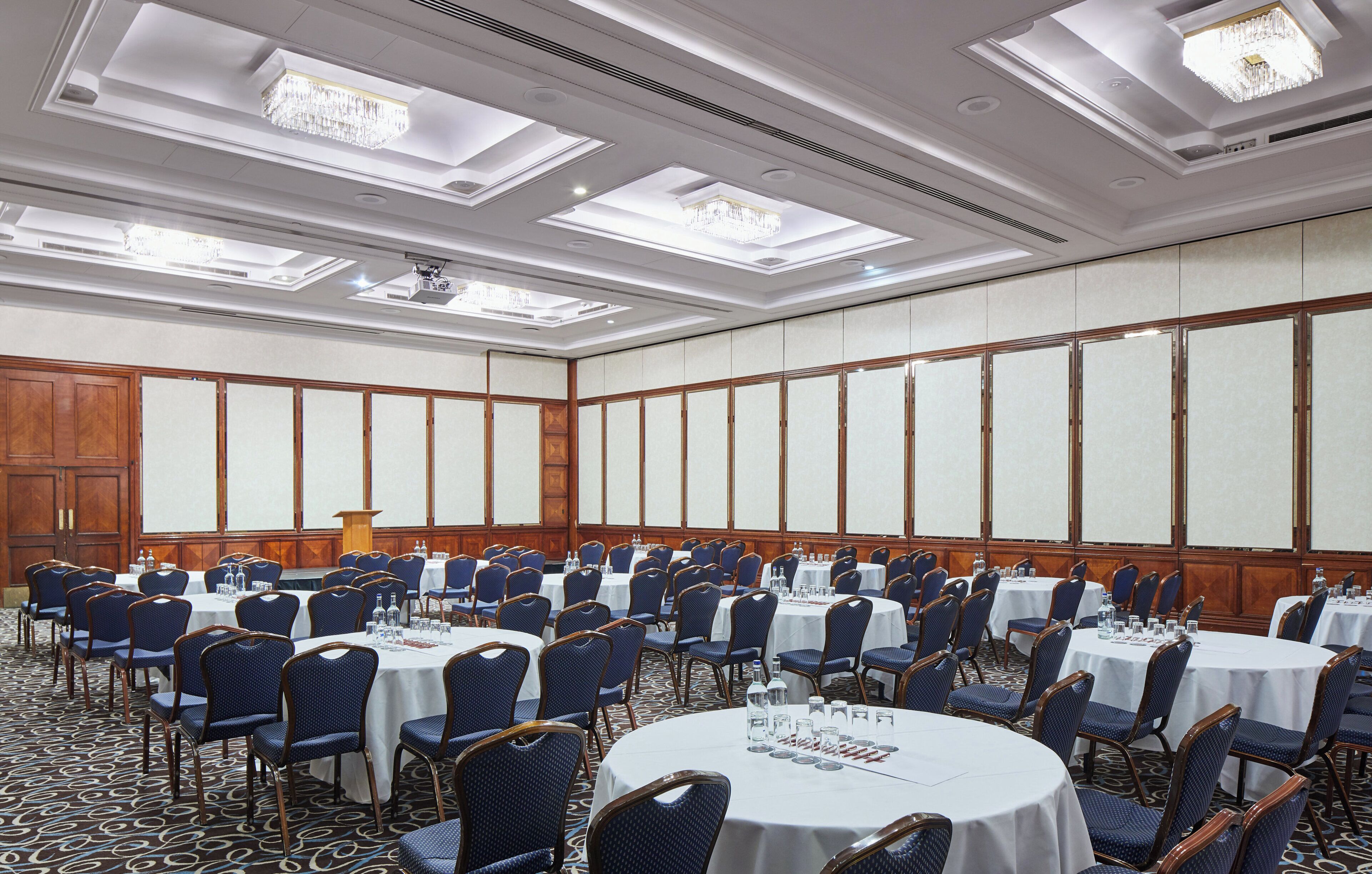 A conference room with round tables, blue chairs, and a podium.