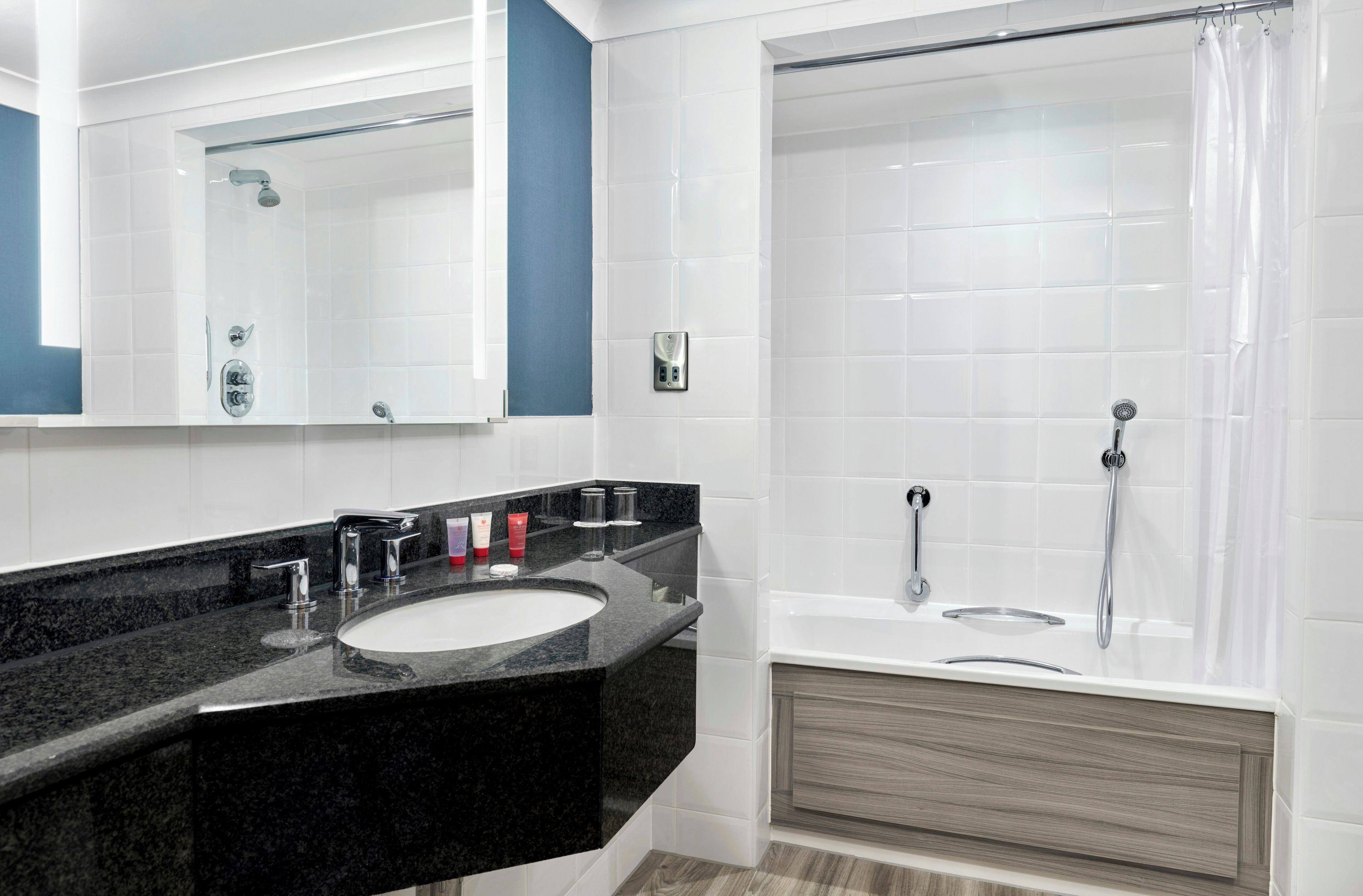 Un baño moderno con un lavabo de granito negro, un espejo grande, una ducha con puerta de vidrio y un mueble de tocador de madera.