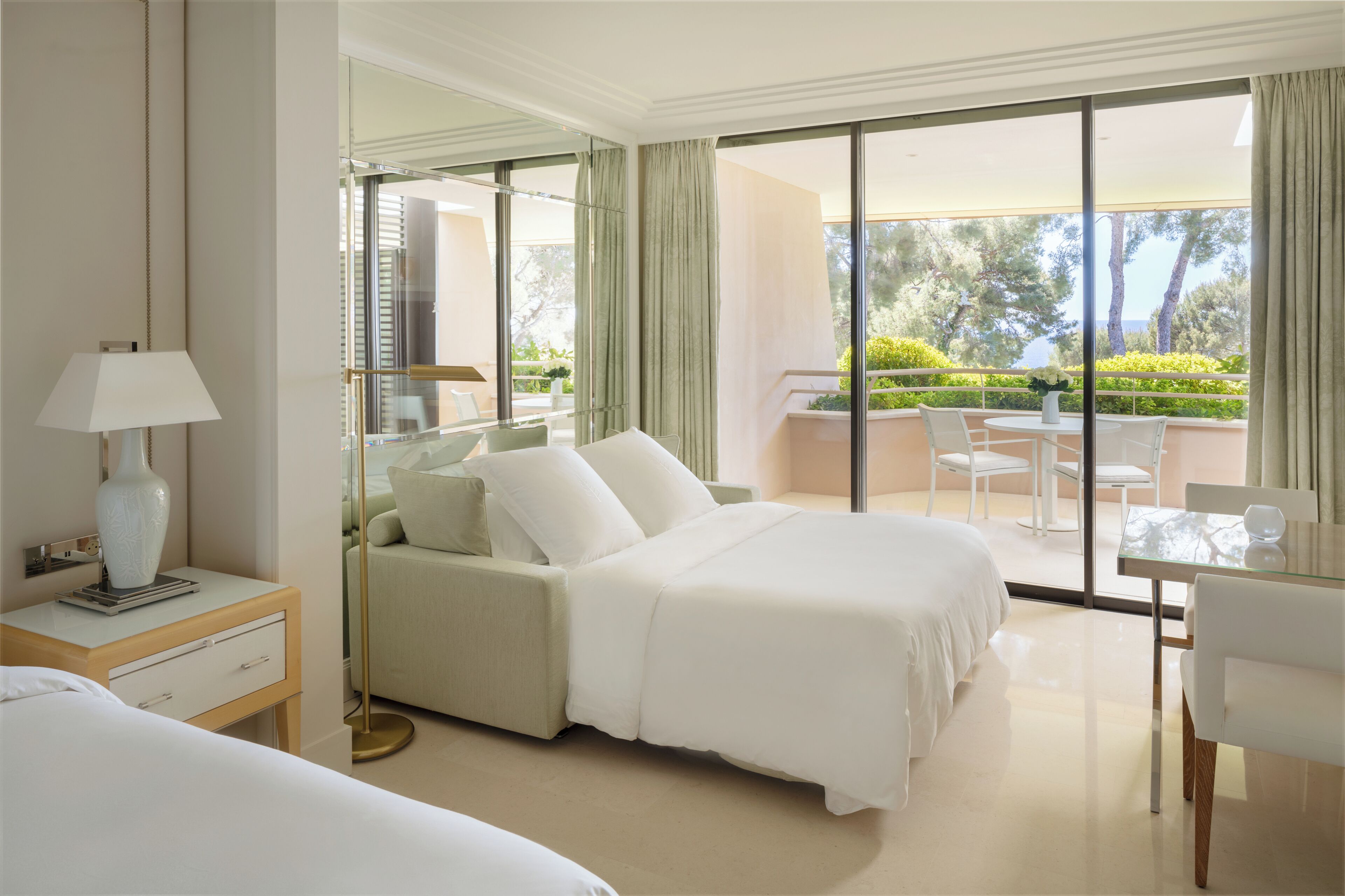 Una habitación de hotel con cama, mesita de noche, lámpara y vista al balcón.