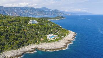 Vue aérienne d’une propriété située sur la côte, avec un grand bâtiment, une piscine et une plage rocheuse.