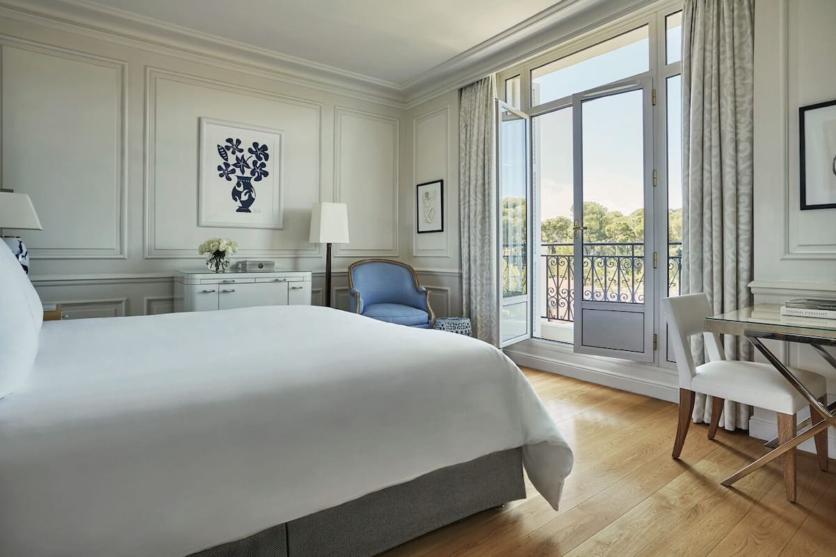 Habitación de hotel con una cama grande, un escritorio, una silla y un balcón con vistas.