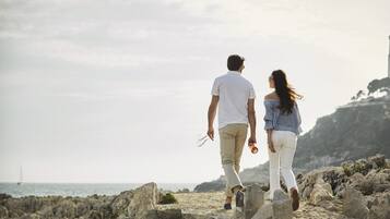 A couple walking on a rocky beach with a view of the sea and a distant sailboat.