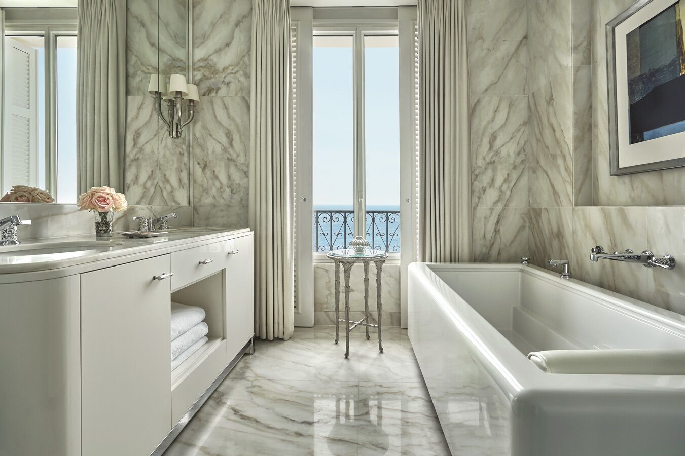 A luxurious bathroom with a marble floor, a large bathtub, and a view of the sea through the windows.