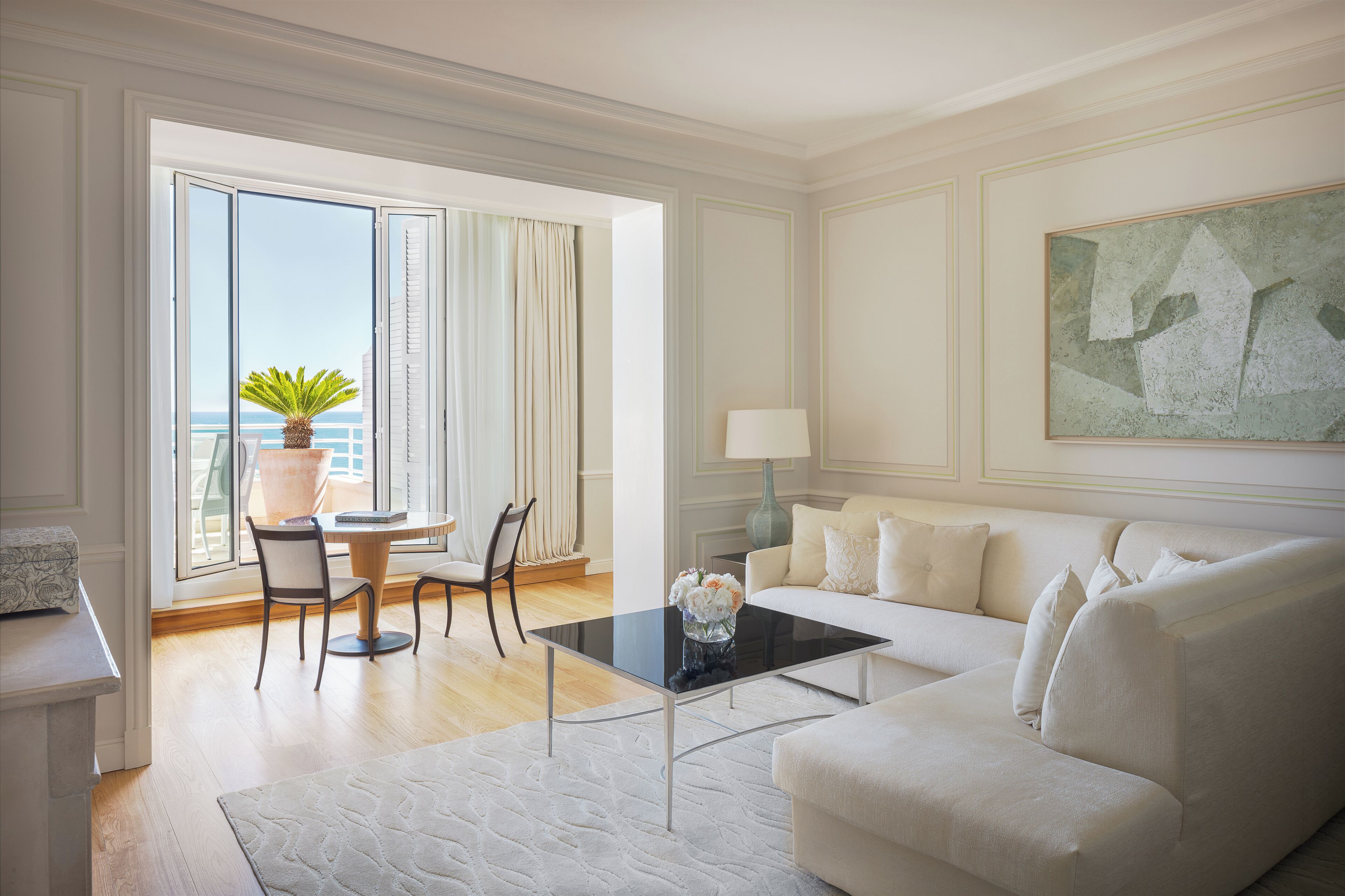 A modern living room with a white sofa, a glass coffee table, and a dining area with a table and chairs.