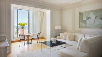 A modern living room with a white sofa, a glass coffee table, and a dining area with a table and chairs.
