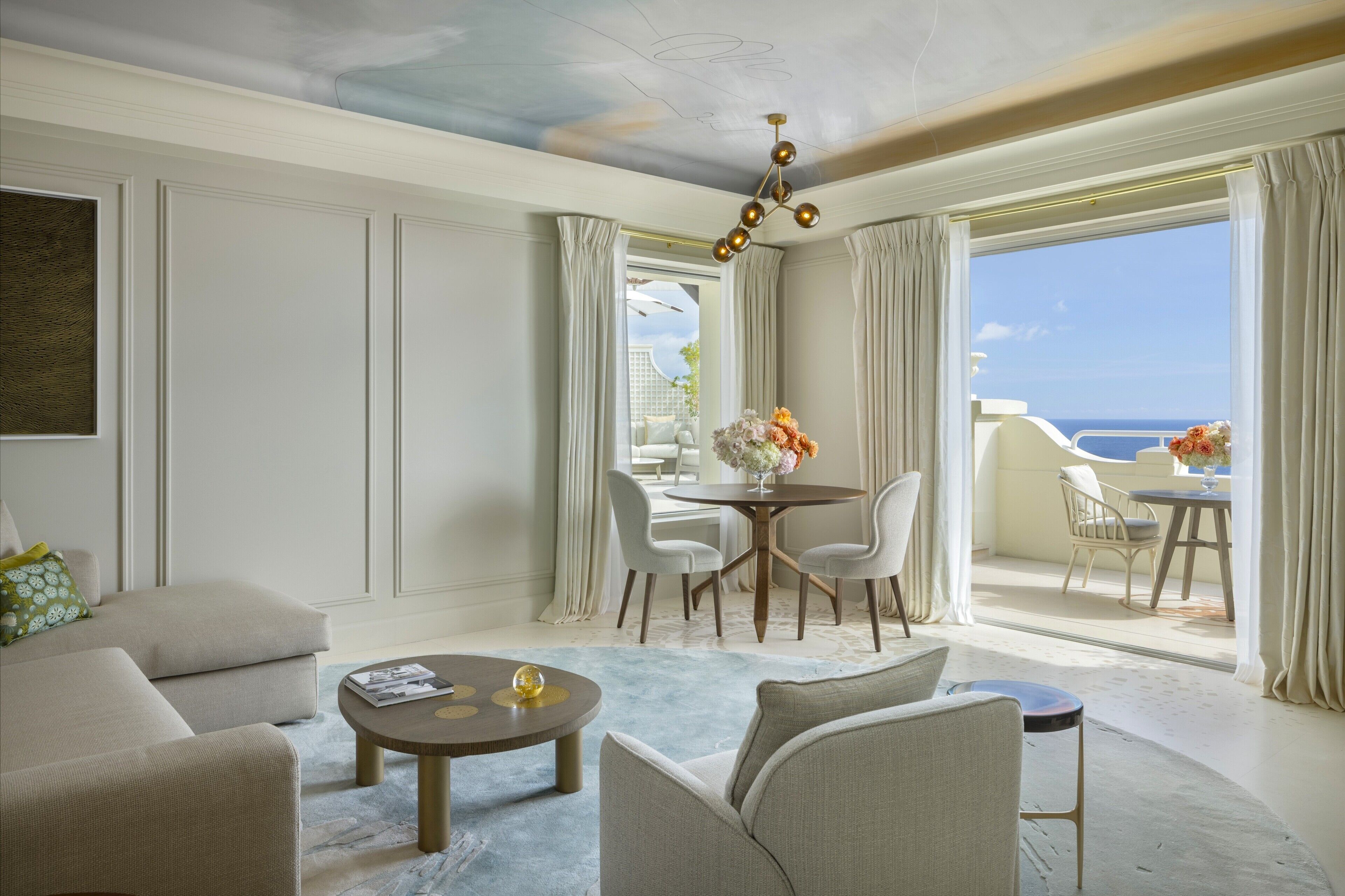 A spacious living room with a large window, a dining area, and a balcony with a view of the sea.