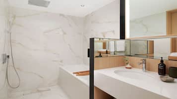 Ein modernes Badezimmer mit Marmorwand, einer Glasdusche, einem weißen Waschbecken und einem großen Spiegel.