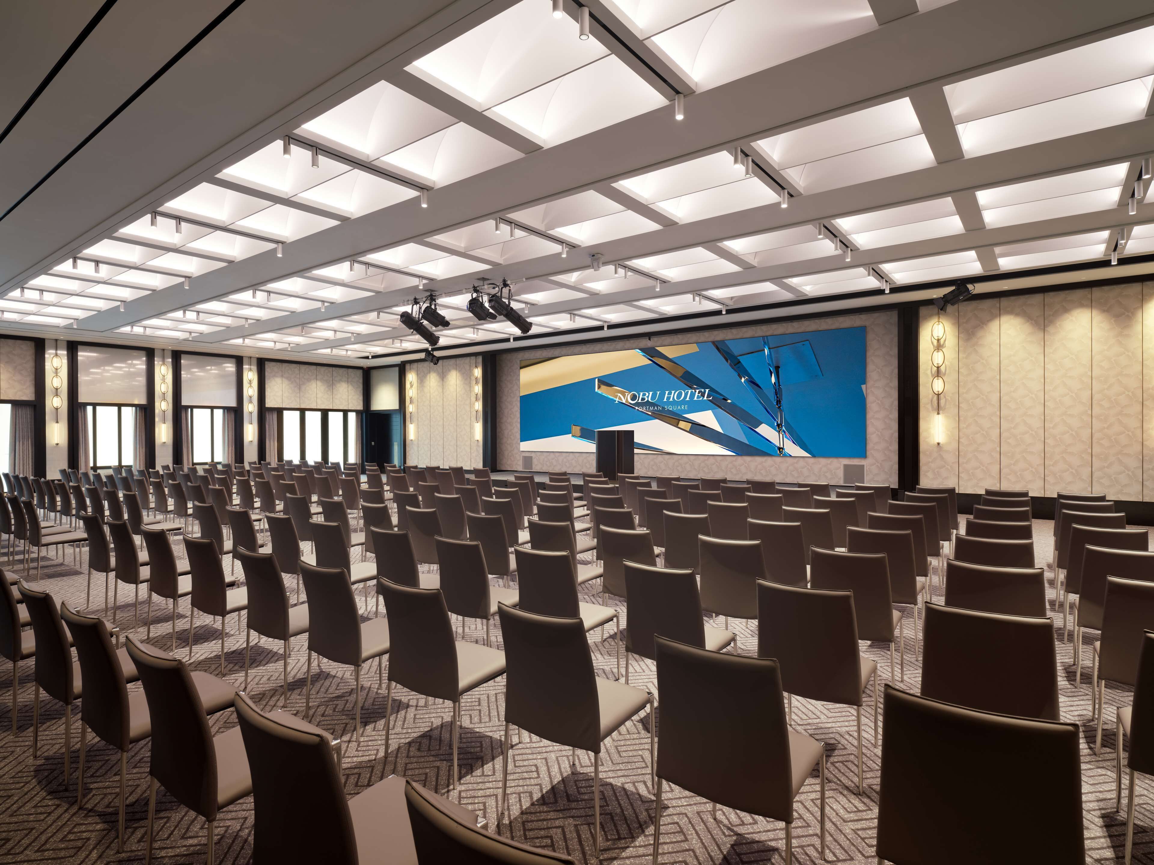 A conference room with rows of chairs, a large screen, and a ceiling with recessed lighting.