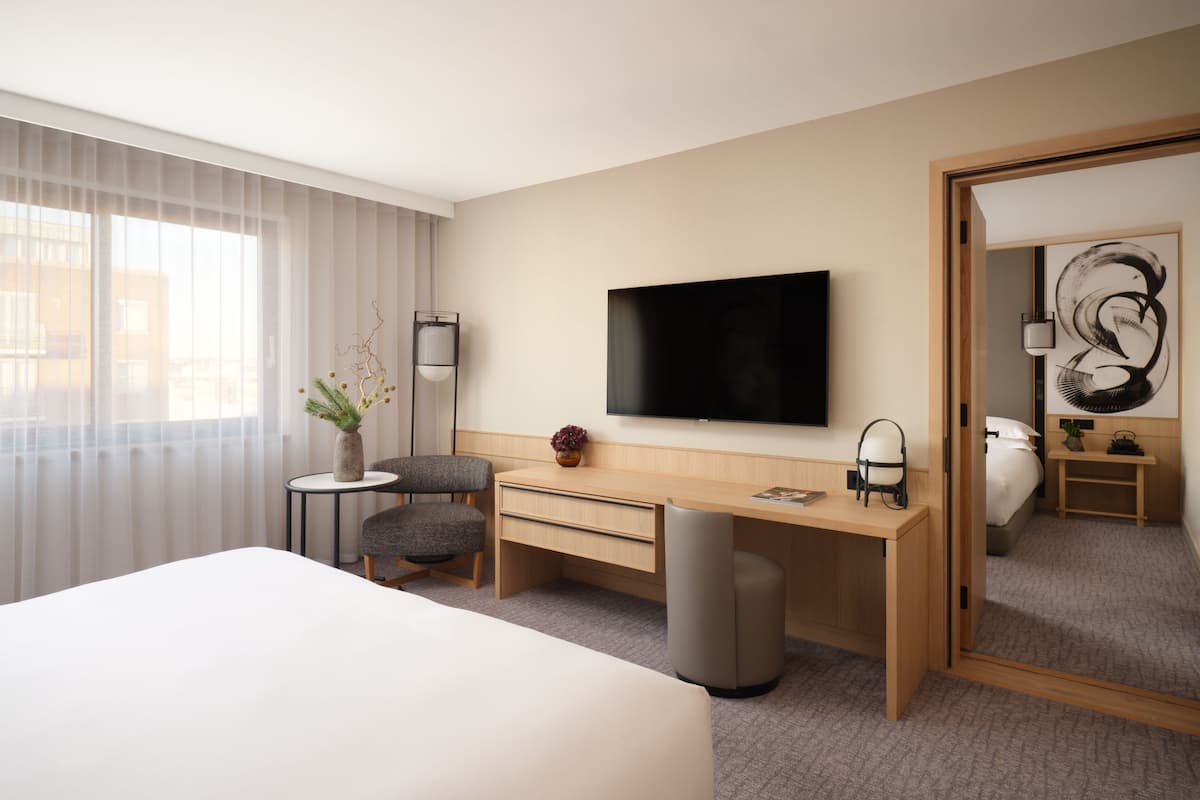 A hotel room with a bed, a desk, a chair, a television, a mirror, and a window with curtains.