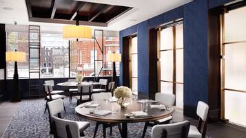A modern conference room with round tables, white chairs, and a large window offering a city view.
