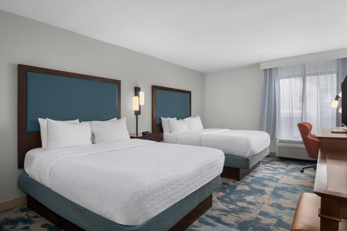 A hotel room with two beds, a desk, and a chair.