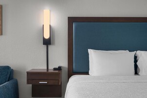 A hotel room with a bed, a nightstand with a lamp, and a blue chair.