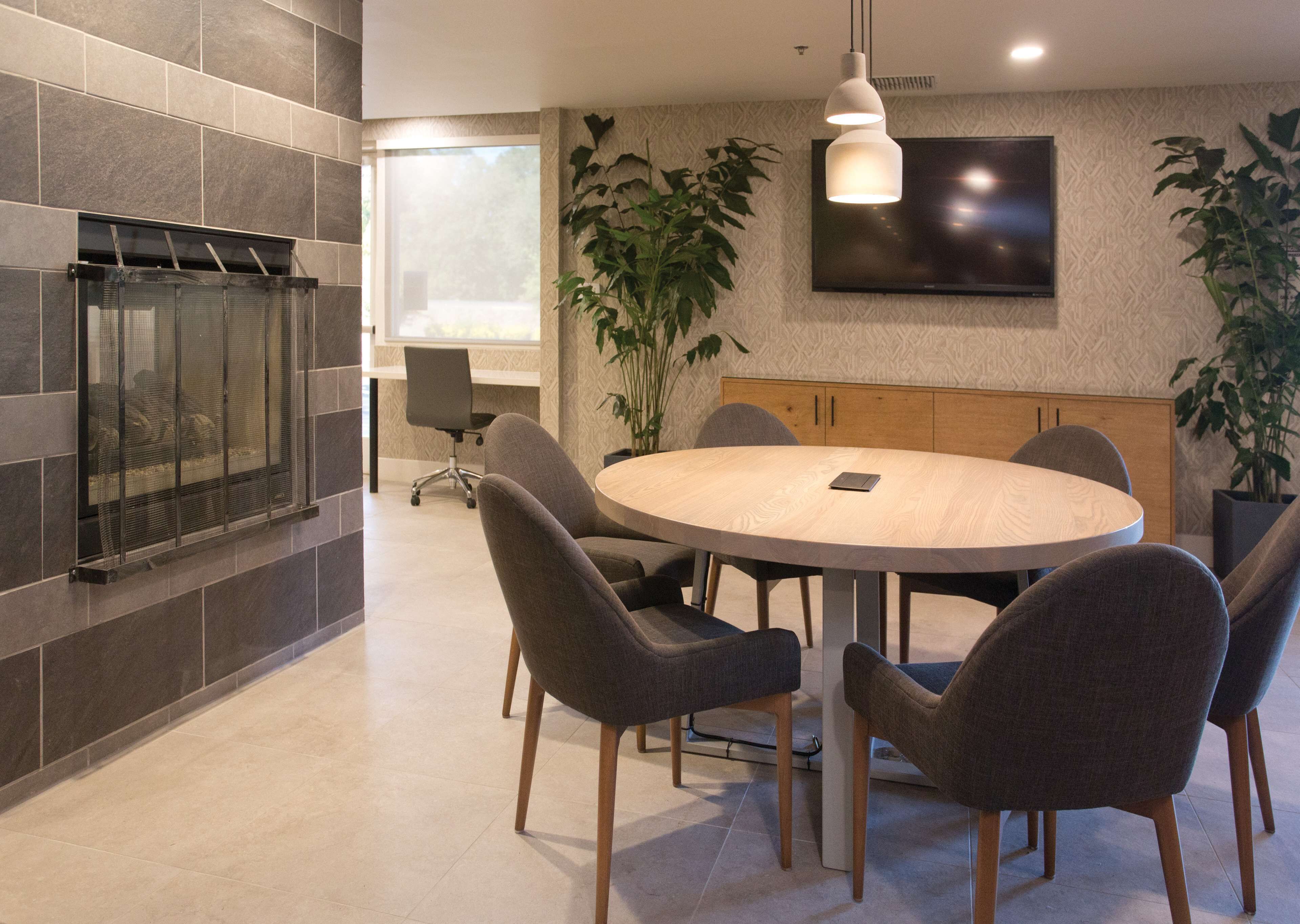 A modern conference room with a round table, six chairs, a television on the wall, and a fireplace.