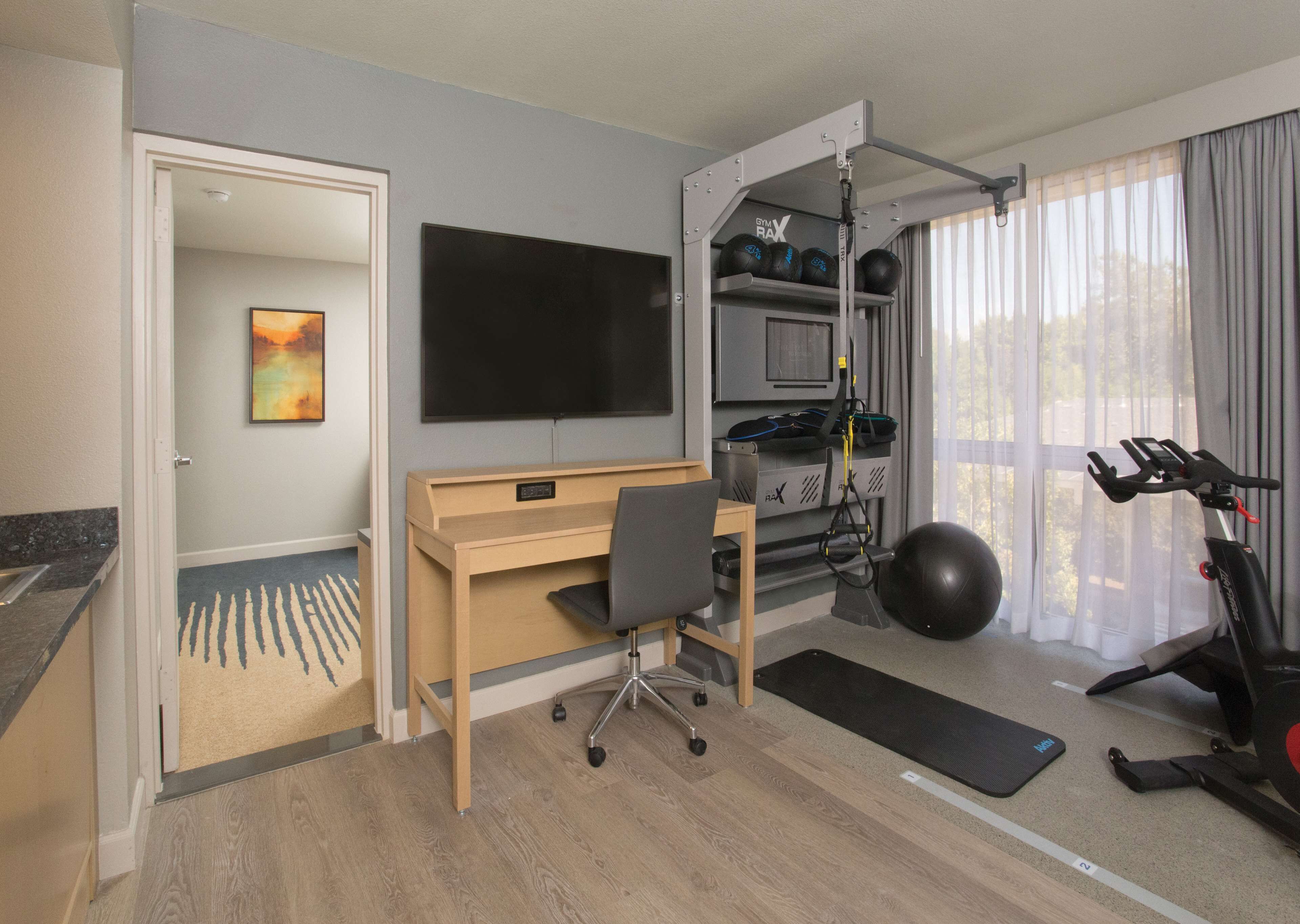 Una camera d'albergo con scrivania, sedia, palla da ginnastica, tapis roulant e televisione.